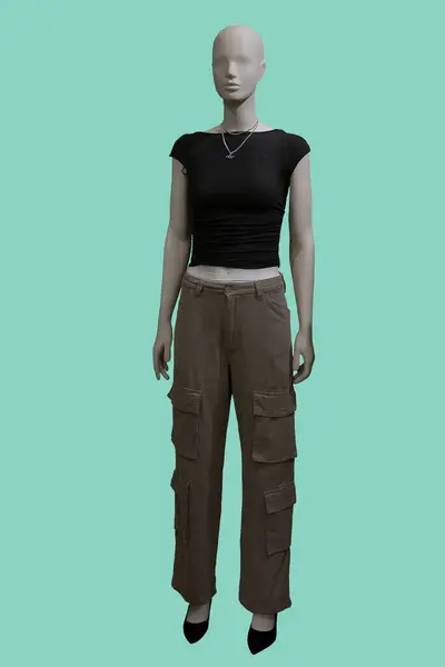 Stock image Full length image of a female display mannequin wearing stylish outfit with black top and light brown cargo pants isolated on green background.