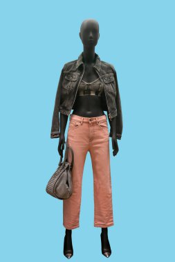 Mavi arka planda gri kot ceket ve pembe kot pantolon giyen bir kadın vitrin mankeni.