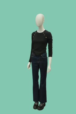 Modaya uygun siyah örgü bluz ve yeşil arka planda izole edilmiş mavi kot giyen bir kadın vitrin mankeni.