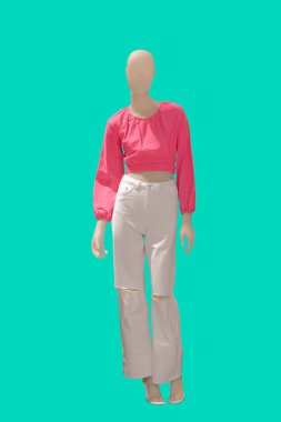 Yeşil arka planda beyaz kot pantolon ve pembe bluz giyen bir kadın vitrin mankeni.
