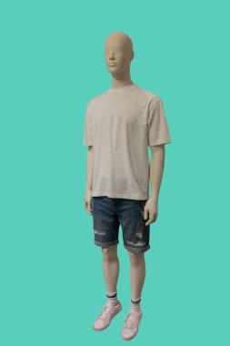 Beyaz tişört giyen ve yeşil arka planda yırtık şort giyen bir erkek vitrin mankeni.