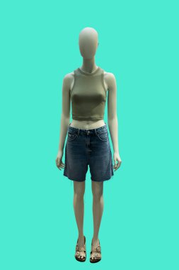 Modaya uygun örgü şort ve mavi kot şort giyen bir kadın vitrin mankeninin tam boy görüntüsü mavi arka planda izole edilmiş.
