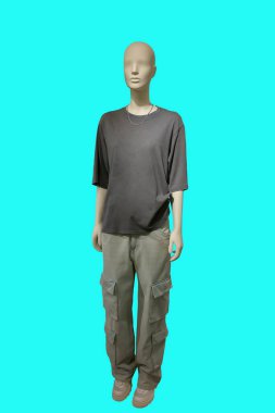 Yeşil arka planda kahverengi tişört ve gri kargo pantolon giyen bir kadın vitrin mankeni..