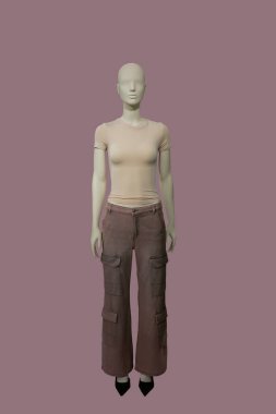 Açık kahverengi tişört ve pembe arka planda izole edilmiş kahverengi kargo pantolon giyen bir kadın vitrin mankeni.