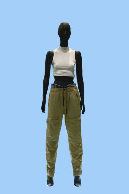 Mavi arka planda kolsuz beyaz bluz ve haki renkli pantolon giyen bir kadın vitrin mankeni.