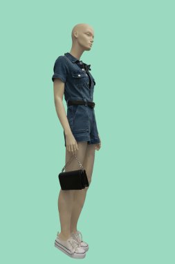 Yeşil arka planda izole edilmiş şortlu şık kot pantolon giyen bir kadın vitrin mankeni.