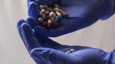 Ellerinde haplar ve kapsüller tutan eldivenler.
