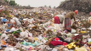 Üç adam çöp alanında işe yarar maddeler aramak için sopa kullanıyor.