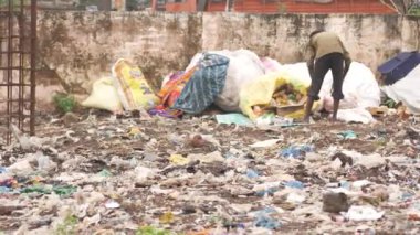 Bir adam elleri çöp öğütücüsünde bir çuvalda pislik temizliyor.