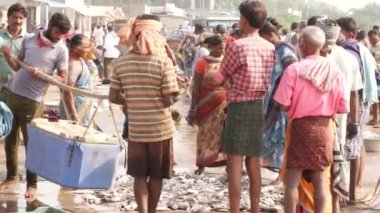 Soğutucuyu taşıyan adamlar sopayla asıldı ve bacağıyla balık paketleyen bir kadın Chirala Balık Pazarı, AP, Hindistan - Aralık 2022