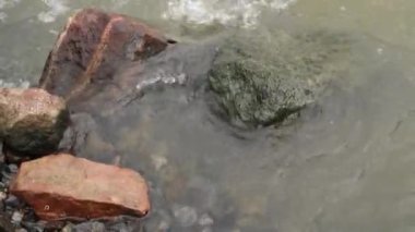 Küçük taşlar ve büyük bir kaya, üzerinde akan nehir suyu.