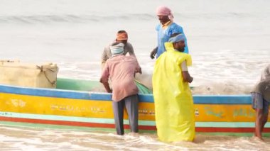 İki adam balıkçı teknesinde, üç kişi de balıkçı teknesinde balık ağları taşımaya çalışıyor.