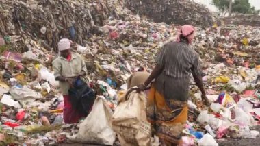 Çöp öğütücüden çıkan bir çuvalda işe yarar şeyler toplayan adamlar.