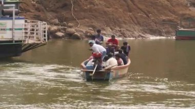 Kayıkçı sandalda kürek çekiyor, yolcular biniyor.