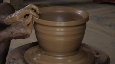man hands shaping a large, spinning clay pot on a pottery wheel.