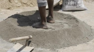 A pair of bare feet mixing a pile of sand and cement.