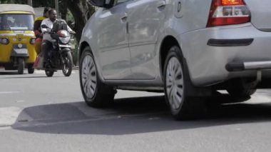 A close-up side view of a cars and scooters on a road.