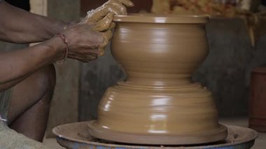 A pair of hands shaping a large, spinning clay pot on a pottery wheel.