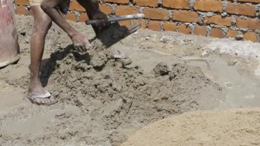 A worker using a trowel to level wet sand or mortar on the ground.