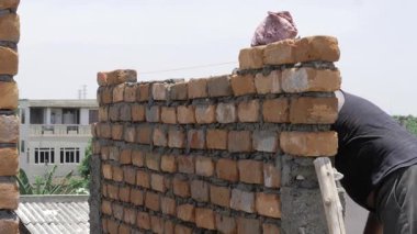 A newly built brick wall with mortar and a bag on top. men working during the day 