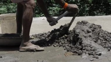 A person mixing cement and sand with a shovel on the ground.