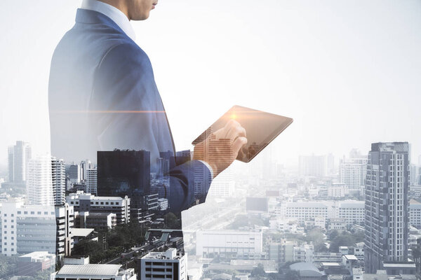 Business technology concept with businessman using modern digital tablet on city skyline background, double exposure