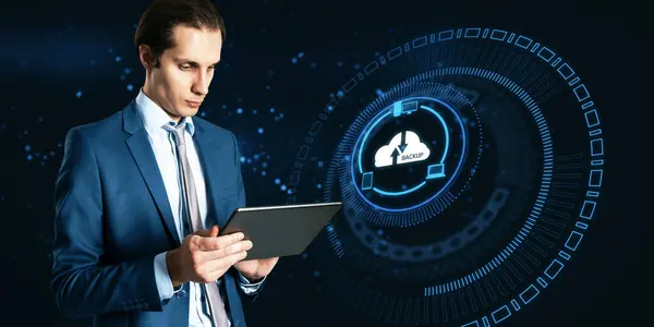 Attractive young european businessman holding tablet with abstract glowing cloud hologram on blurry dark background. Cloud computing, big data backup concept