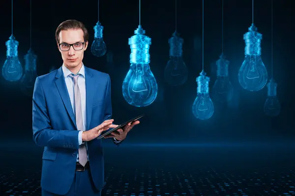 Attractive young european businessman using mobile phone with glowing digital lamp hologram on dark background. Idea, innovation and future concept