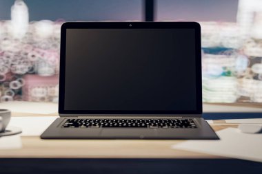 Boş siyah modern dizüstü bilgisayar ekranının ön görüntüsü logonuz ya da açık ahşap yüzeyde pencere arkasından bulanık şehir görüntüsü, yakın plan. 3B görüntüleme, modelleme