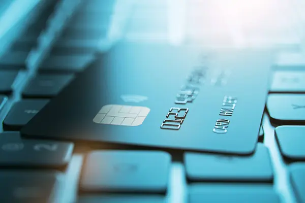 Online banking concept with dark color credit card on blurred laptop keyboard background, closeup. 3D rendering
