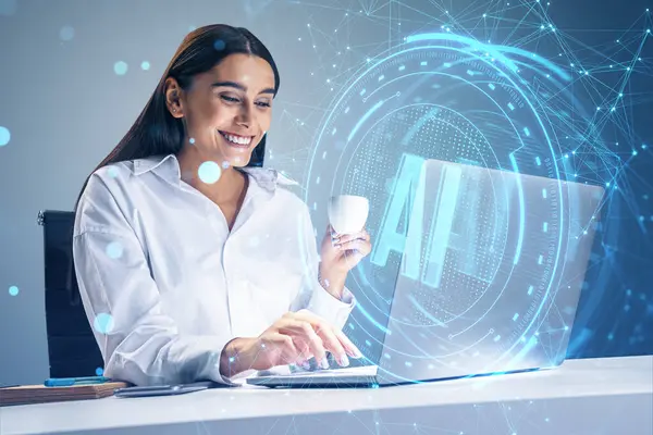 Happy young businesswoman with coffee cup using laptop at desk with glowing blue AI hologram on blurry background. Artificial intelligence, technology and innovation concept