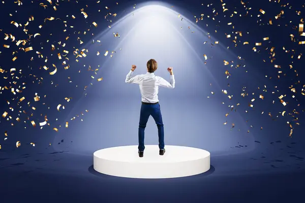 stock image Man in a business suit celebrating on a podium under a spotlight with confetti. Dark background. Concept of success and victory