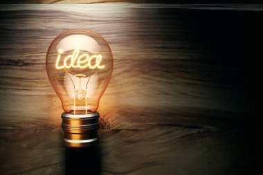 Illuminated lightbulb with the word idea glowing inside, standing against a wooden background. Concept of creativity and innovation. 3D Rendering clipart