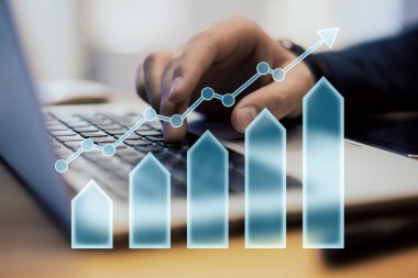 Closeup of a hand typing on a laptop, with a transparent arrow and bar chart overlay on a blurred background. Concept of business growth and financial success