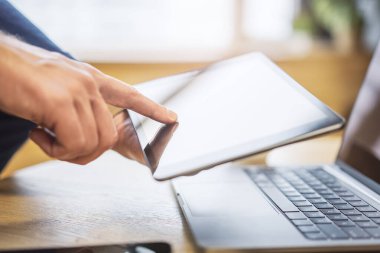 Male finger gently tapping the screen of a sleek digital tablet lying on a desk, within the unfocused brightness of a contemporary office clipart