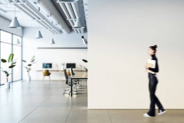 A businesswoman holding documents walking in a modern office. Blurred motion. Office space with desks, plants, and large windows clipart