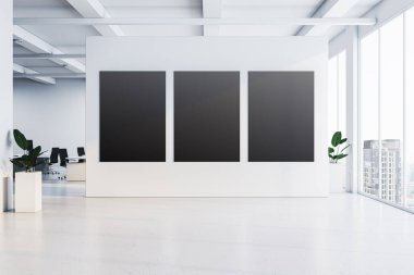 Beyaz bir duvarda üç boş poster, büyük pencereler ve şehir manzaralı parlak ofis alanı. Minimalist tasarım, temiz çizgiler ve doğal ışık. 3B Hazırlama.