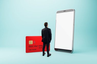 Takım elbiseli bir işadamı, büyük akıllı telefon ve ışık eğimli arka planda kırmızı kredi kartının önünde dikiliyor. Mobil bankacılık kavramı