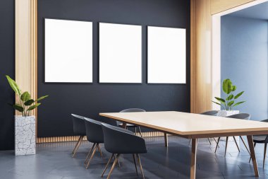 Modern ofis toplantı odasında, tahta masa, sandalye ve bitkilerle dolu karanlık duvarda üç dikey boş poster çerçevesi. 3B Hazırlama