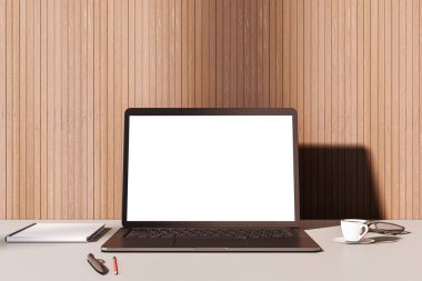 Temiz bir masada boş beyaz ekranlı dizüstü bilgisayar, ahşap duvar arka planı, yanında kahve fincanı ve defter, çalışma alanı sunumu konsepti. 3B Hazırlama.