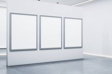 Modern galeri içinde beton zemin ve yumuşak ışıklandırmalı beyaz bölme duvarında üç boş gümüş çerçeveli poster. 3B Hazırlama