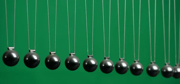 Newton\'s cradle physics concept for action, reaction or cause and effect. Balls Newton on green background