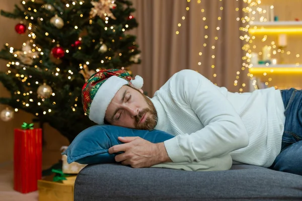 Чоловік Втомився Різдво Одягнений Новорічний Капелюх Спить Біля Ялинки Сидить — стокове фото