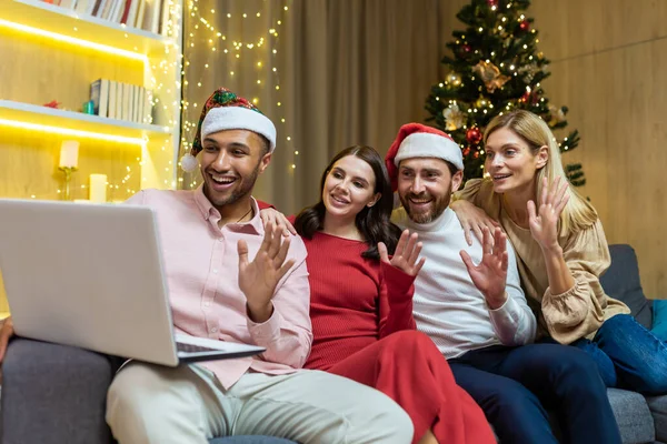 diverse friends celebrating New Year and Christmas together home, Christmas party with guests, men and women smiling and happy together talking on video call greeting friends remotely, using laptop.