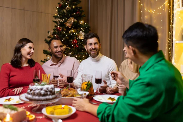 stock image Friends celebrate Christmas eve or New Year holiday paty together sitting at the table. Feast at home group of multi ethnic festive christmas dinner. happy cheerful people clink wine glasses laugh