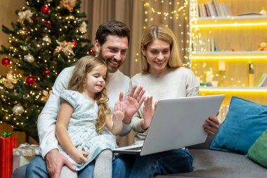 Noel 'de aile arkadaşlarıyla ve internet üzerinden selamlaşmalar ve görüntülü arama yapan ailelerle konuşuyor. Erkek ve kız, Noel ağacının yanındaki koltukta oturup uzaktan iletişim kurmak için dizüstü bilgisayar kullanıyor..