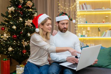 Genç çift evde birlikte çalışıyorlar, dizüstü bilgisayarlarıyla mutfakta oturuyorlar, birlikte mutlular, yılbaşı ve Noel tatilleri boyunca..