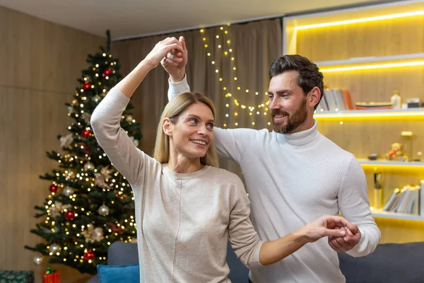 Family couple in love dances and hugs at Christmas, man and woman celebrate New Year together at home near the Christmas tree.