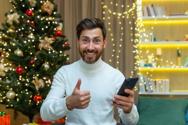 Noel 'de bir adam kameraya bakar ve parmağını doğruluğu kanıtlanmış bir şekilde tutar. Yılbaşı tatili için Noel ağacının yanındaki kanepede oturur..