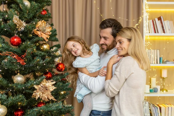 Christmas and new year family decorate tree, man woman and child daughter at home together in living room for new year smile and rejoice, happy family holidays.
